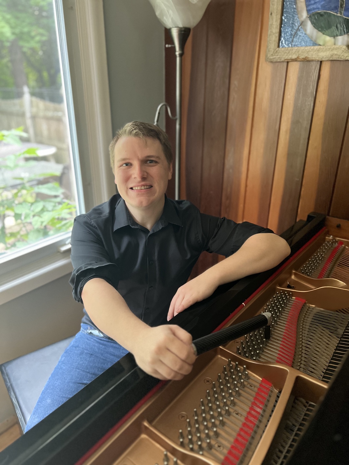 Alan Lynch seated at a grand piano with a tuning lever